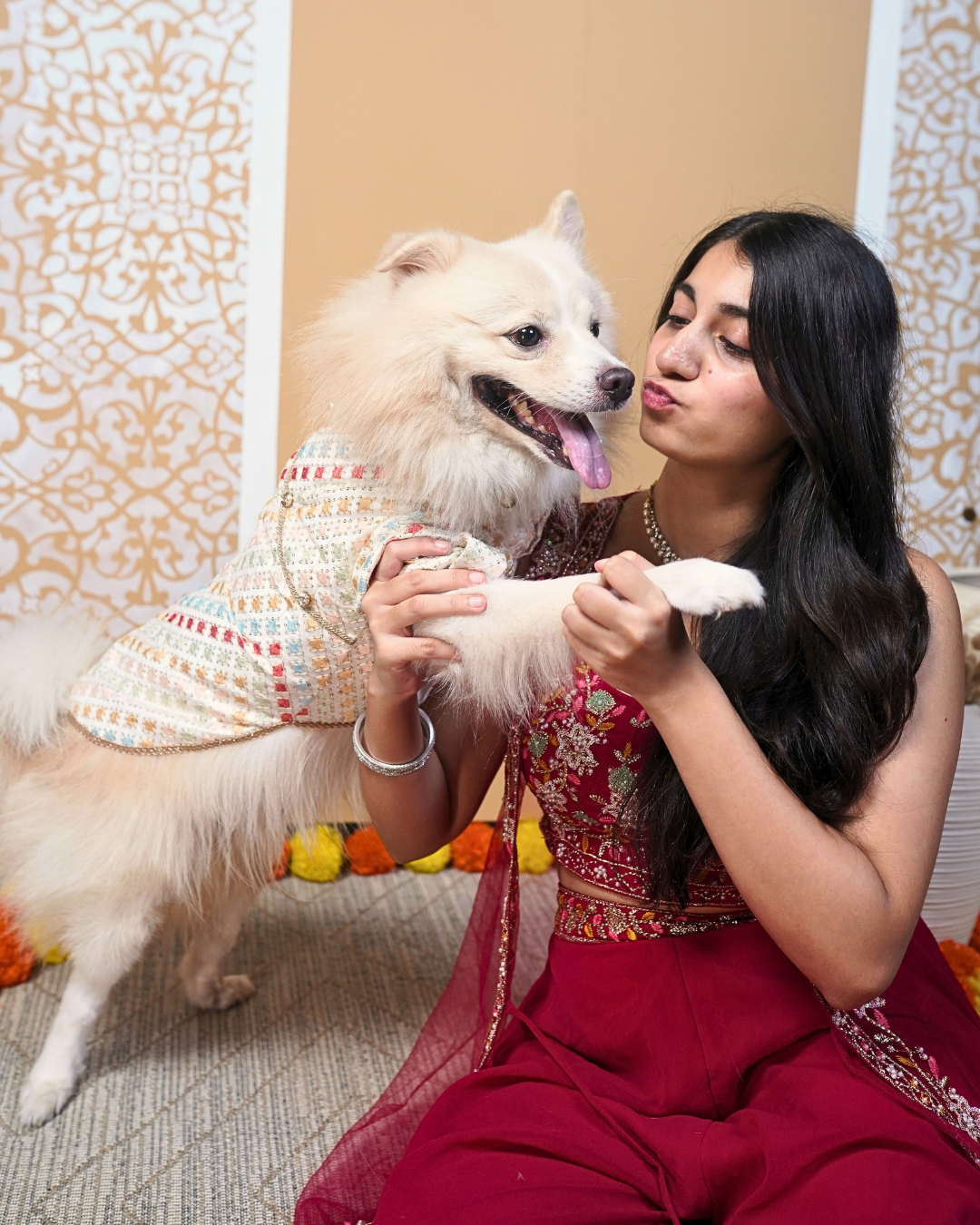 Woman in a red outfit with an Indian Spitz wearing the Satrangi dog kurta